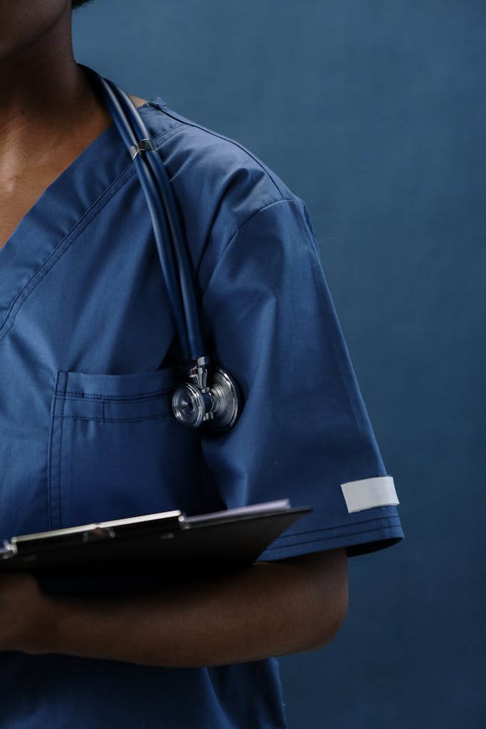 Close-up of a healthcare professional in blue scrubs with a stethoscope and clipboard.