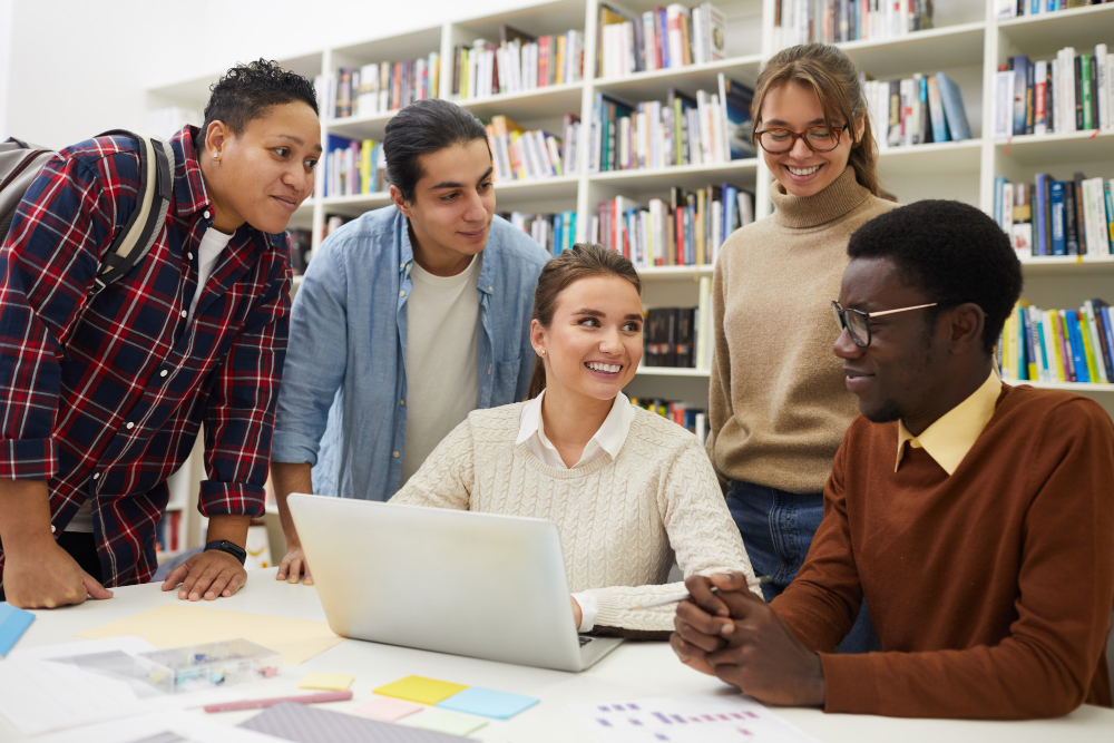 Students collaborating around a laptop in a library.