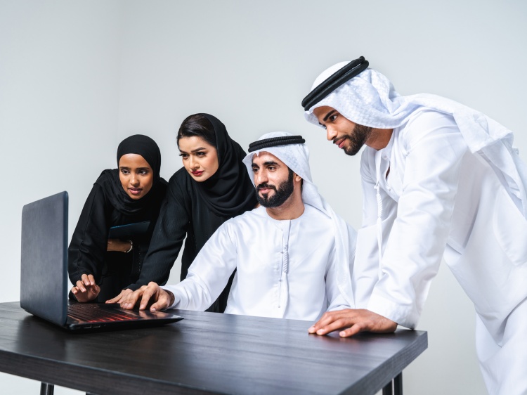 Four Emirati professionals collaborating around a laptop.
