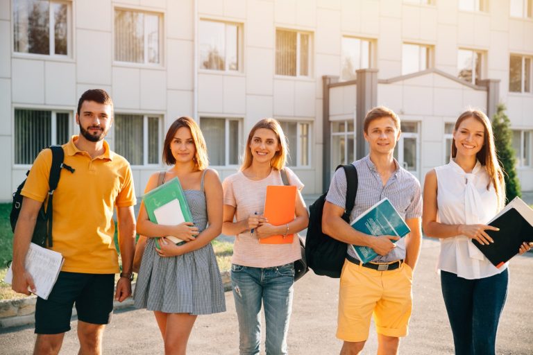 Young adults holding books outside an educational building.
