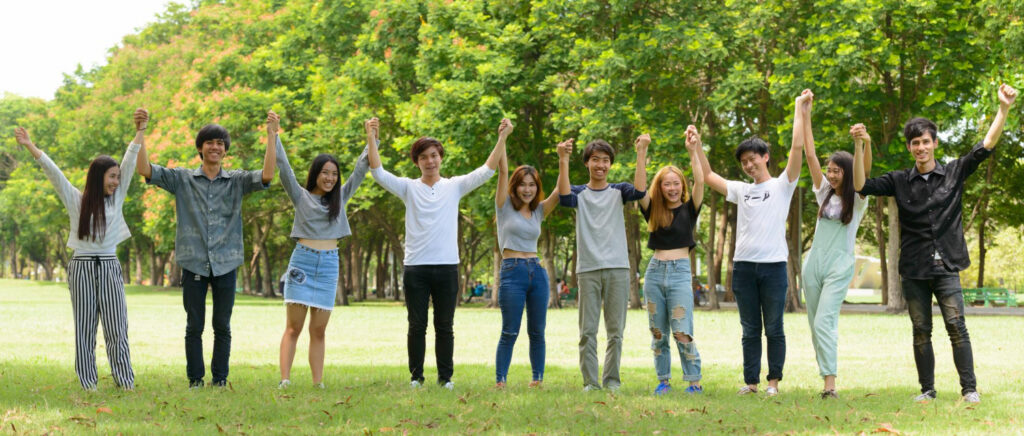 Young people standing together in a park with their hands raised