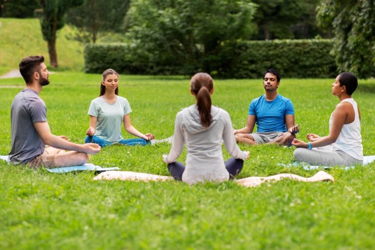 A group meditating together on grass in a park.