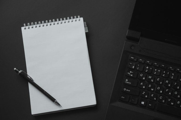 A notebook and pen beside a laptop.