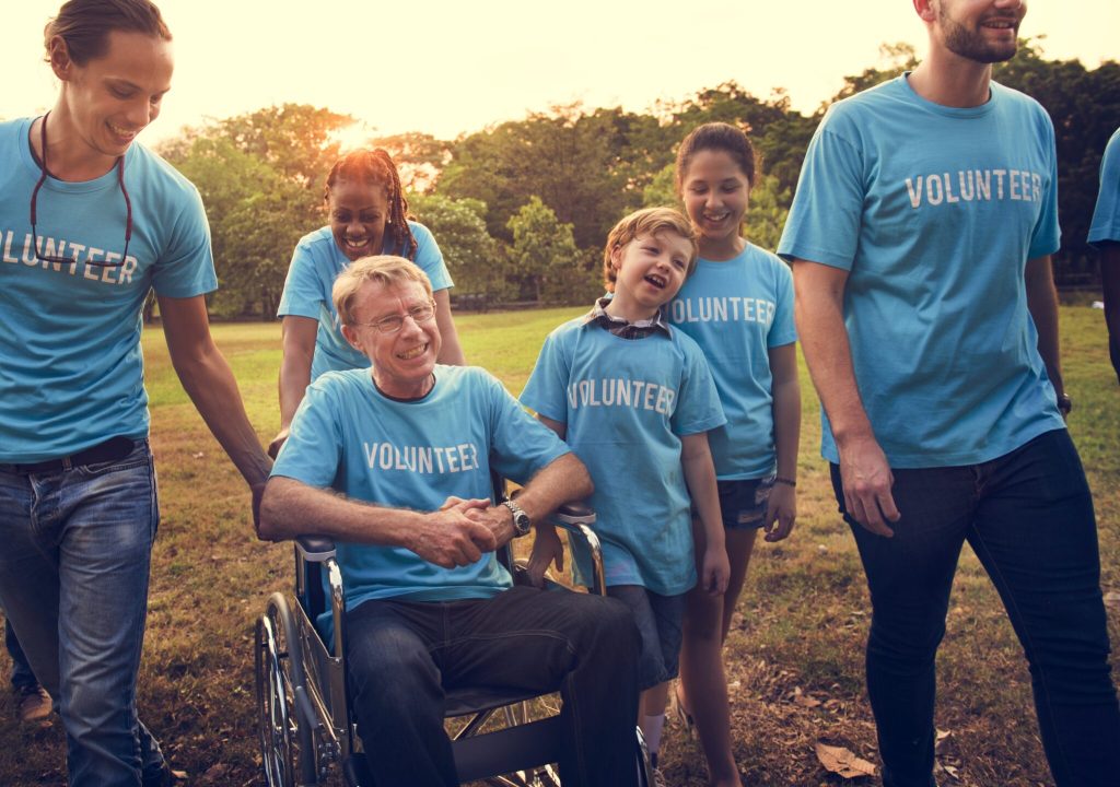 Volunteers, including a wheelchair user, gathered outdoors in a park.