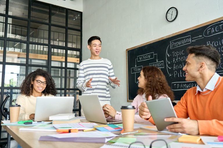 Young adults collaborating around a table with laptops and notebooks.