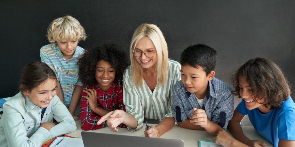 A female school teacher sitting at a table with students.