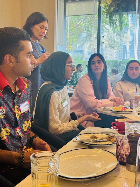 A student shares an idea while peers listen around the table.