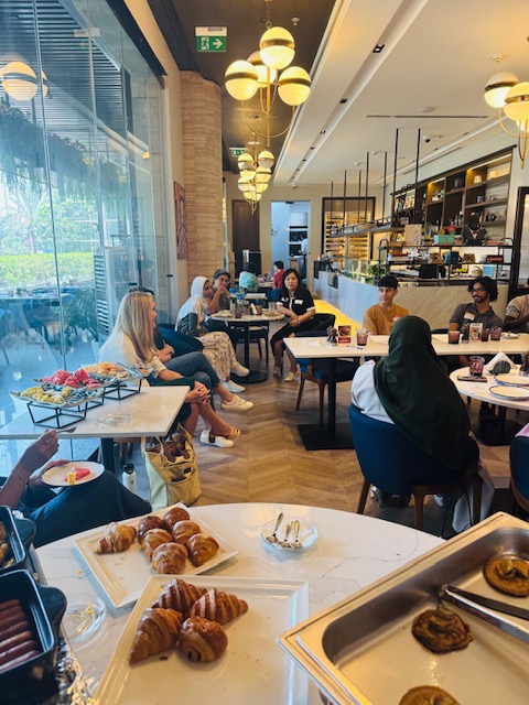 A workshop circle meets in a bright cafe setting with shared notes and refreshments.