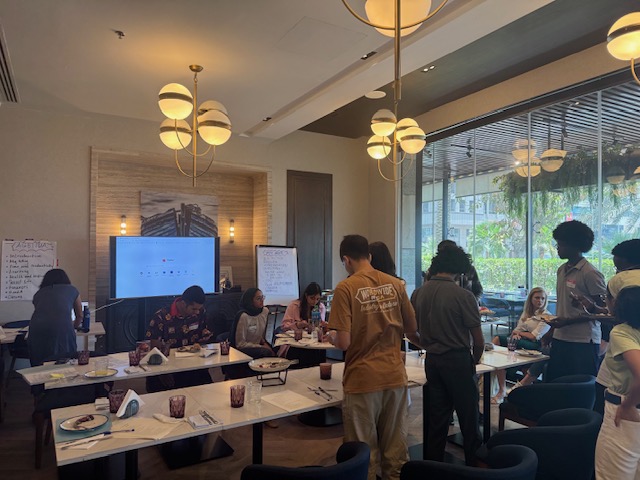 Students and mentors work around cafe tables during a collaborative session.